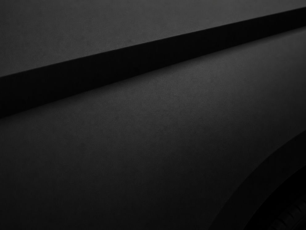 A dark car panel in matte black film, the light diffused across it